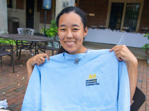 A student holds up a blue shirt that says "Transfer Students Connected"