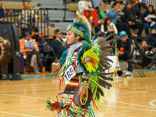 A young boy in regalia finishes his dance during a competition