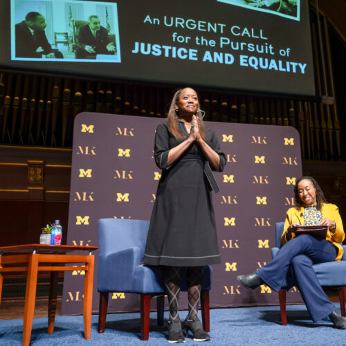 Erika Alexander on stage at Hill Auditorium with her hands clasped in gratitude to the audience