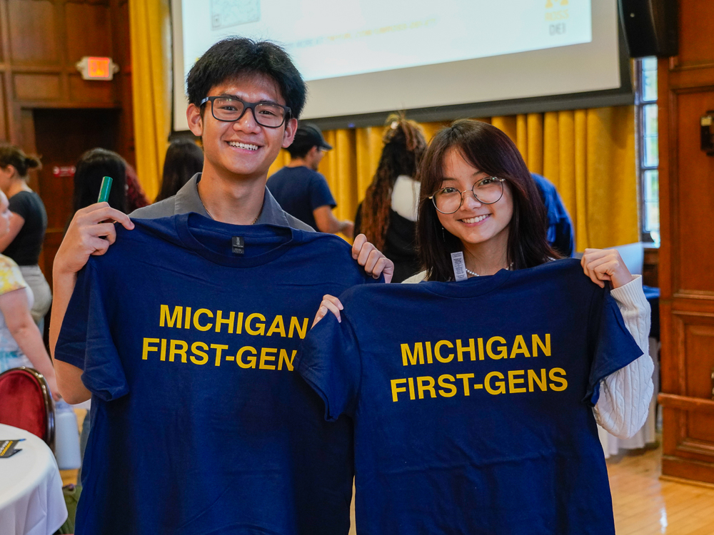 Two students smile and hold up 'Michigan First-Gen' shirts